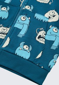 Blaues Sweatshirt mit einem Muster aus Cartoon-Monstern mit einzelnen Augen und Accessoires. Das Material ist weich und hat einen gerippten Saum sowie Ärmelabschlüsse.