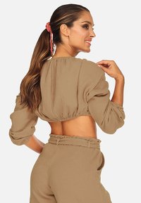 Brązowy krótki top z bufkami i marszczonym dołem. Gładki, fakturowany materiał. Noszony z pasującymi spodniami o wysokim stanie, z paskiem.