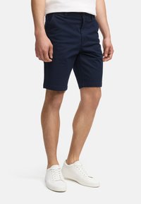 Shorts en coton bleu marine à coupe droite, dotés de passants de ceinture et de poches latérales, associés à des baskets blanches.