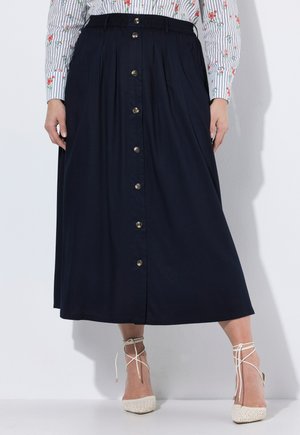 Frau trägt einen midilangen marineblauen Rock mit vorderen Knöpfen, kombiniert mit einem gestreiften Blumenhemd und weißen Schnürabsätzen.