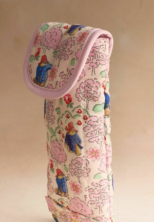 Tikkikangasranneke, jossa on violetti reunus ja kuvituksena siniseen takkiin ja punaiseen hattuun pukeutunut karhu vaaleanpunaisten puiden ja kukkien keskellä.