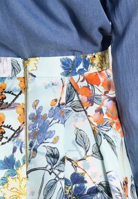 Blommönstrad kjol med en ljusblå bas, som har orange, lila och gröna accenter. Fållad design med dragkedja bak.