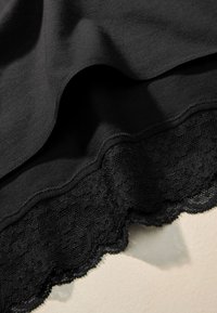 Fekete szövetfüggönyök sima textúrával, alul hullámos csipke szegéllyel. A csipke részletes mintázattal és áttetsző megjelenéssel rendelkezik.