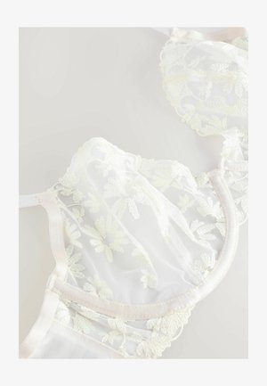 Valkoinen pitsirintaliivi, jossa on kukkakirjontaa, läpikuultavat verkokupit, satiiniset hihnat ja soikeat reunat. Kevyt, hienovaraisilla teksteillä ja yksityiskohdilla.