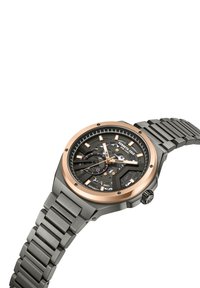 Rund klocka med en svart skelettskiva, roséguld bezel och ett mattsvart metallarmband med länkdesign. Inkluderar kontrasterande timmarkeringar.