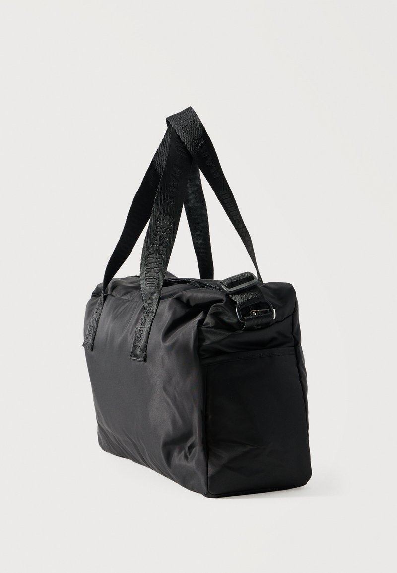 Black rectangular soft fabric tote bag with long branded handles and a zipper closure on top, shown at a slight angle.