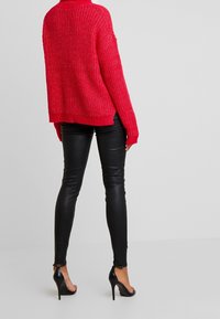 Röd, kraftigt stickad tröja med hög krage och oversized ärmar, ihop med slanka svarta läderleggings och svarta högklackade skor.