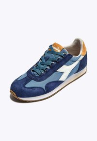 Sneaker in suede blu navy con accenti in tessuto blu chiaro, logo bianco e suola in gomma marrone; presenta lacci piatti e un inserto sul tallone in contrasto color sabbia.