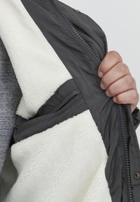 Gray jacket with a white fleece lining, featuring a front zipper, interior pocket, and textured, soft fabric.