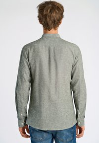 Langsleeve, groene gestructureerde shirt met een kraag, knoopmanchetten en een achterplooidetail, gedragen met blauwe denim jeans.