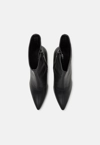 Botas de tobillo de cuero negro con un diseño de punta afilada, cremalleras laterales y detalles de costura, con una textura suave y una silueta elegante.