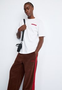 White cotton t-shirt with red text on the chest, paired with brown corduroy pants featuring red side stripes and an adidas logo.