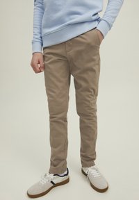 Bruna chinos i bomull med slim fit och sidofickor. Matchas med vita sneakers och en ljusblå sweatshirt.