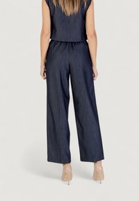 Džíny s širokým střihem v tmavě modré barvě, s elastickým pasem a uvolněným střihem, doplňující cropped top styl.