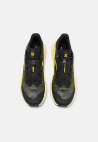 Baskets de course noires et jaunes avec une tige en maille texturée, des rayures contrastées et une semelle légère et amortissante. Les lacets sont noirs.