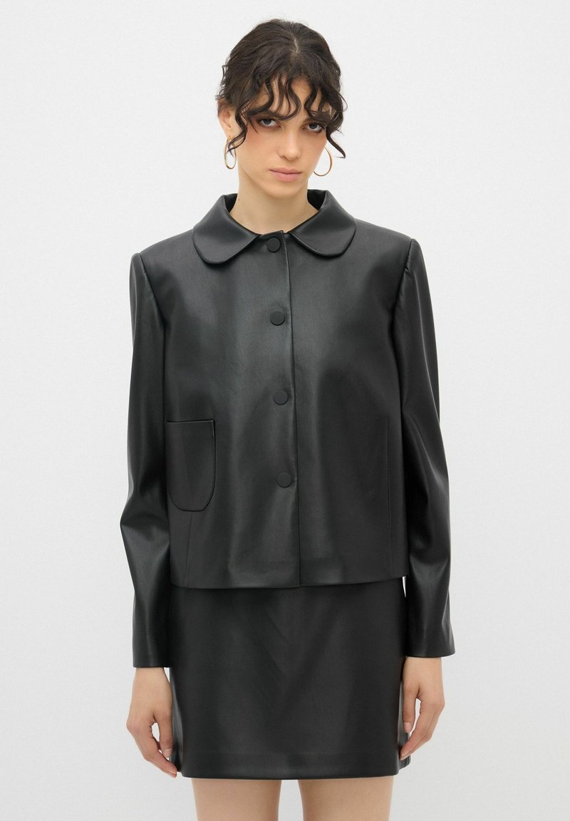 Schwarze Kunstlederjacke mit runden Kragen, Frontknöpfen und einer einzelnen Tasche. Glatte Textur und enganliegende Silhouette.