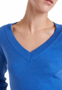 Suéter de punto azul con diseño de cuello en V. La tela parece suave con una textura lisa. La silueta ajustada resalta la línea del cuello.