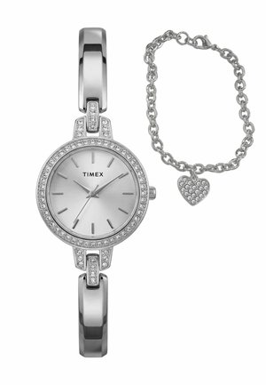 Orologio Timex argento con lunetta tempestata di cristalli e maglie a barra, abbinato a un braccialetto a catena argento con un ciondolo a forma di cuore di cristallo.