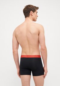 Black boxer briefs with a red elastic waistband featuring the Puma logo, minimalist design, and smooth fabric texture.