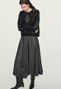 Maglione nero con motivo a rombi, abbinato a una gonna grigia svasata. Stivali neri fino al ginocchio creano un contrasto. Texture lisce in tutto.