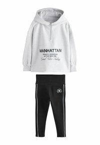 Grau-farbener Kapuzenpullover mit Reißverschluss, versehen mit schwarzem Text und einer Kängurutasche; kombiniert mit schwarzen Leggings mit weißen seitlichen Streifen und Logo.