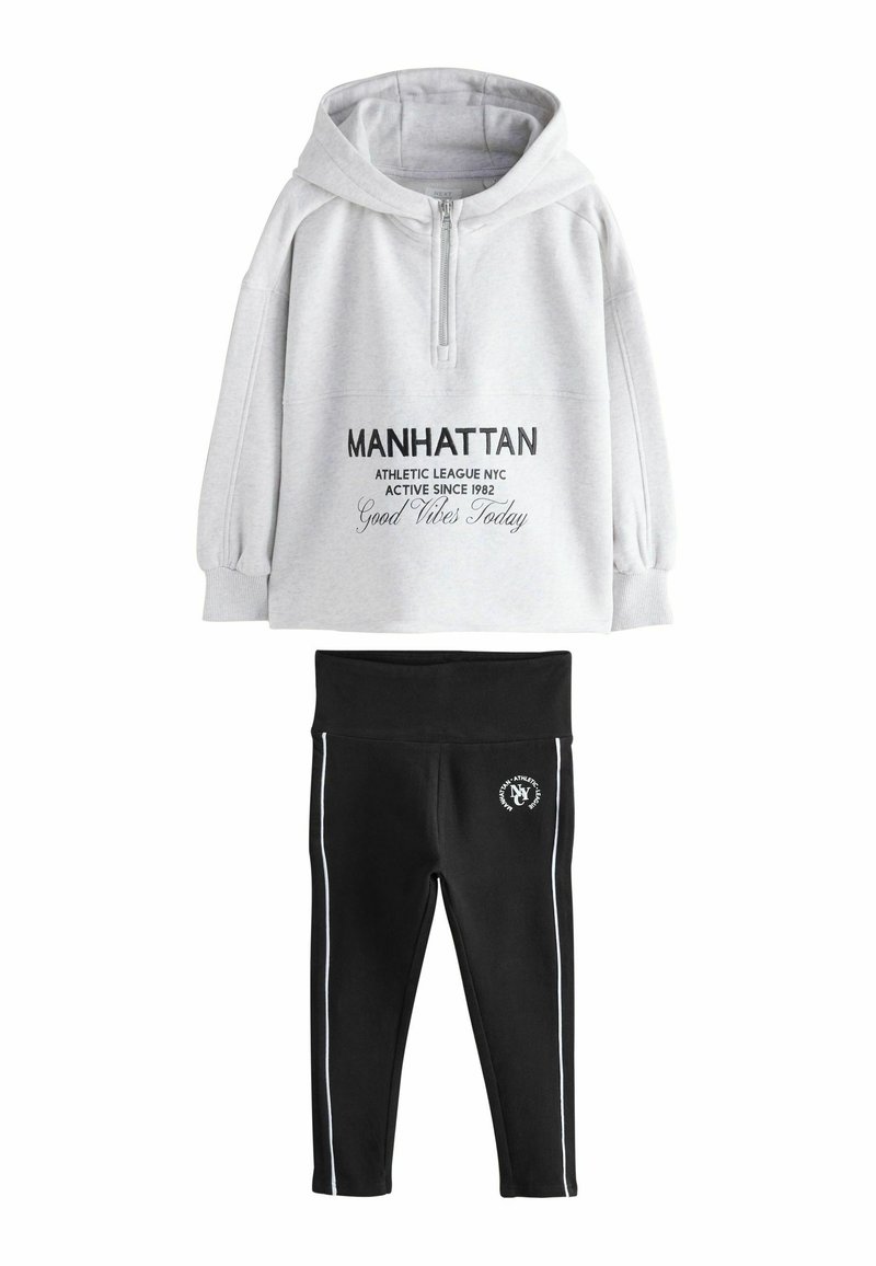Grau-farbener Kapuzenpullover mit Reißverschluss, versehen mit schwarzem Text und einer Kängurutasche; kombiniert mit schwarzen Leggings mit weißen seitlichen Streifen und Logo.
