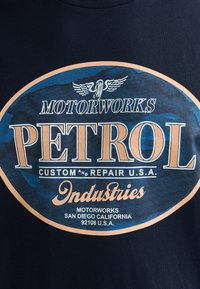Navy blue t-shirt featuring a graphic oval logo in blue and orange. Text includes "Motorworks Petrol" and "Custom and Repair U.S.A."