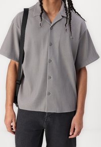 Kortärmad grårandig skjorta med knapp-up design och krage, tillsammans med mörka jeans och en axelremsväska.