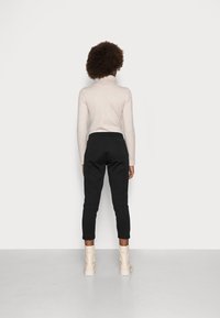 Světle béžový rolák a černé zúžené kalhoty s jemnou texturou, doplněné krémovými kotníkovými botami. Minimalistický design na bílém pozadí.