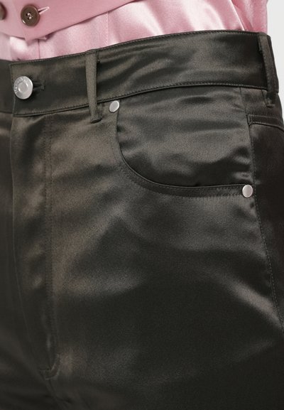 I pantaloni in satin nero presentano un design attillato, tasche frontali con accessori in metallo argentato e una superficie liscia e lucida. La vita è elegante e strutturata.