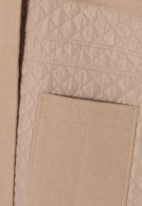 Béžová prošívaná látka s měkkou texturou, obsahující hladký panel a náprsní kapsu. Povrch je texturovaný s diamantovým vzorem.