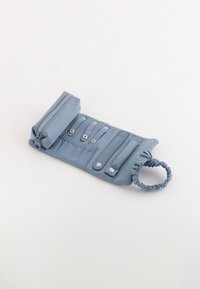 Funda de tela azul clara con cremallera, botones a presión y correa elástica para la muñeca. Cuenta con múltiples compartimentos para organización. Textura suave.