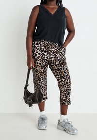 Haut sans manches noir avec un col en dentelle, associé à un pantalon cropped à imprimé léopard. Les accessoires comprennent un sac à épaule noir et des baskets grises.