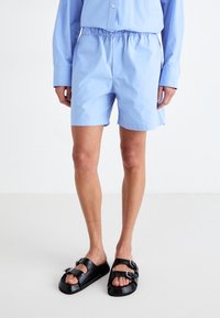 Shorts bleu clair en tissu lisse avec une taille élastique. Assortis à des sandales noires à boucles avec un design texturé.