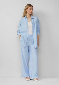 Hellblaues, knöpfbares Hemd aus strukturiertem Stoff, kombiniert mit passenden, leichten, weiten Hosen und weißen Sandalen. Einfaches Design.