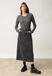 Szary prążkowany longsleeve z guzikami, zestawiony z ciemnoszarym dżinsowym spodnicą z wysokim stanem. Modelka nosi czarne platformy i prążkowane skarpetki.