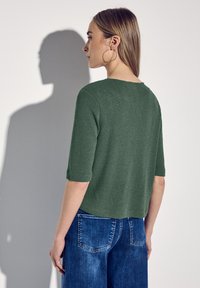 Pull en tricot vert à manches courtes et col rond, associé à un jean bleu avec un design classique à cinq poches.