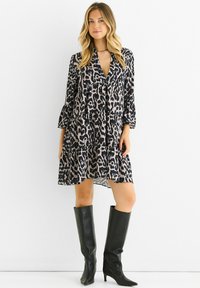 Leopard print dress with a deep v-neck, tiered design, long sleeves, and a flowing silhouette; paired with knee-high black leather boots.