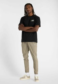Camiseta negra con un logo, pantalones beige ajustados y zapatillas ligeras. El conjunto presenta un ajuste relajado y puños elásticos en los pantalones.