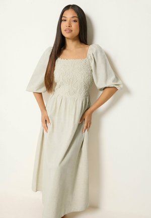 Mujer con cabello largo y liso que lleva un vestido beige claro con mangas abullonadas y bordado floral en el corpiño.