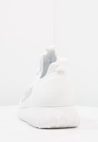 Vit sneakers med övre i meshtyg, rund häl och texturerad sula. Logotypen syns som präglad text på h älen. Dragflik på baksidan.