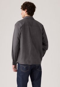 Grijze langemouwenshirt met een kraag, van een gemêleerde stof en met knoopmanchetten, gecombineerd met donkergene jeans met kenmerkende stiksels op de achterzak.