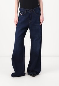 Laiad tumepruunid denim- teksad kõrge vööjoonega, viie taskuga, kontrastõmbluste ja nupulukuga. Sile tekstuur.