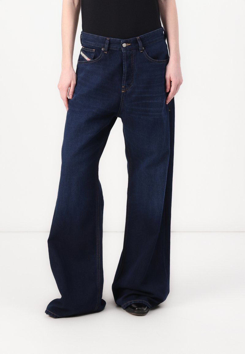Laiad tumepruunid denim- teksad kõrge vööjoonega, viie taskuga, kontrastõmbluste ja nupulukuga. Sile tekstuur.