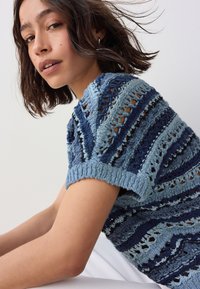 Blaues und hellblaues Strickoberteil mit gestreiftem Muster und Durchbruchdetails, kurzen Ärmeln und gerippten Bündchen. Strukturierte Oberfläche.
