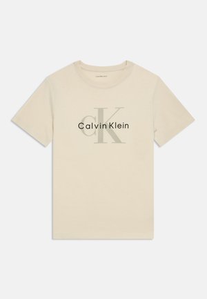 Beige bomull T-shirt med rund halsringning. Har ett stort grått tryck av "CK" och "Calvin Klein" som visas tydligt. Korta ärmar.