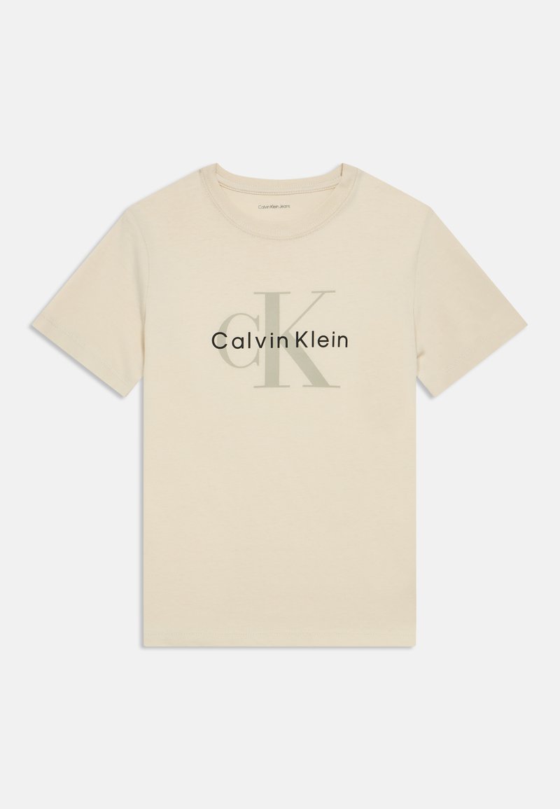 Beige színű pamut póló kerek nyakkal. A "CK" és a "Calvin Klein" nagyméretű szürke nyomtatással látható rajta. Rövid ujjú.