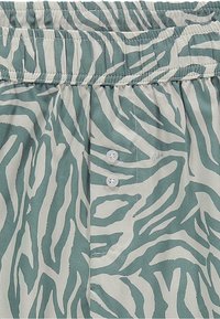 Bluza sa uzorkom zebra u tirkiznoj i bijeloj boji, s rastezljivim pojasom i tri bijele dugmadi za zatvaranje.