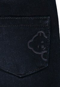 Svart denimficka med en subtil präglad björndesign. Stygn är synliga l�ängs kanterna och visar på noggrant hantverk.