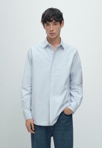 Jasnoniebieska koszula z kołnierzykiem, z długimi rękawami i luźnym krojem, zestawiona z ciemnoniebieskimi dżinsami. Gładka, wypolerowana faktura materiału.
